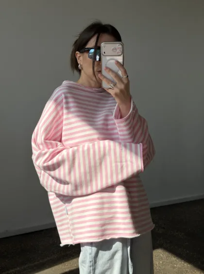 Person in an oversized pink and white striped sweater takes a mirror selfie while wearing dark sunglasses and silver jewelry.